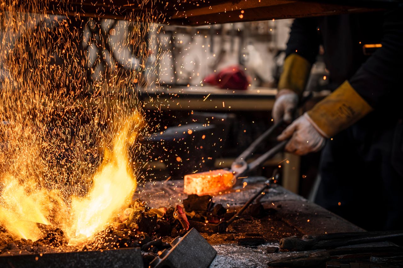 our-story-02 Blacksmith working with hot metal in fiery forge, sparks flying.